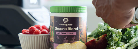 A tub of Amazing Grass Greens Blend Antioxidant Sweet Berry on a cutting board with fresh fruit
