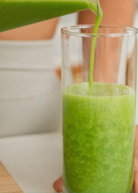 Green smoothie being poured into a glass with a blurred background