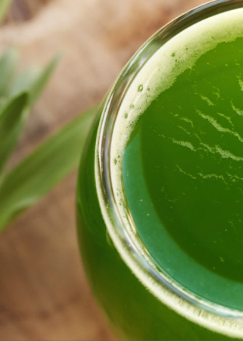 Close-up of a glass filled with green juice on a wooden surface.