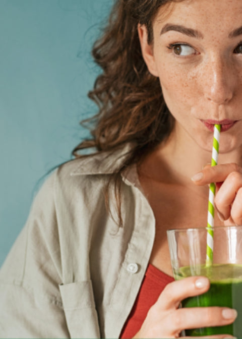 Woman drinking a green smoothie with a straw against a teal background