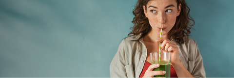 Woman drinking green juice from a glass with a straw against a blue background