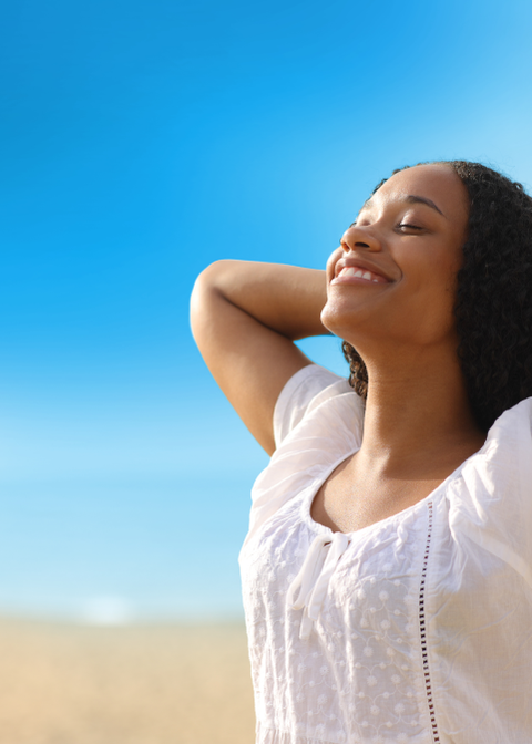 Woman smiling with her arms behind her head toward the blue sky