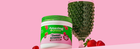 glass of green juice next to Amazing Grass Sweet Greens powder against a pink background